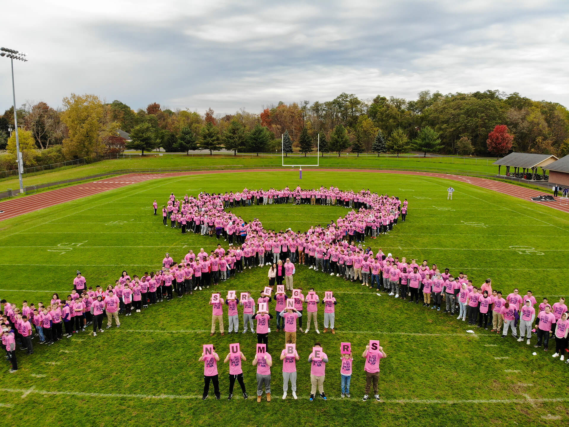 Large group standing on an athletic field in the shape of a ribbon.